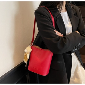 Detail of red litchi texture leather bucket bag with a cute teddy bear plush charm