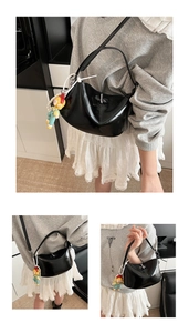 Detail of glossy black hobo bag with silver turn-lock and cute doll pendant charm