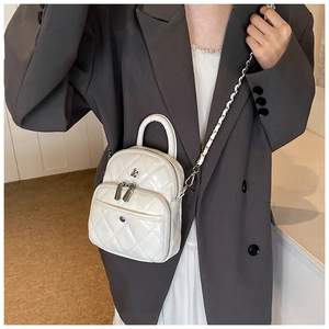 Gros plan d'un mini sac à dos blanc matelassé avec fleur en métal et bandoulière chaîne