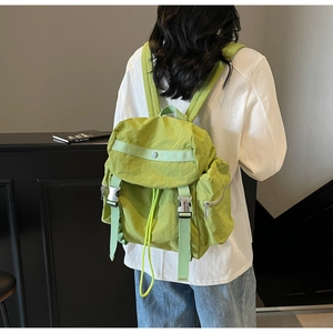 Light green nylon backpack with flap closure and metal buckles shown on a model