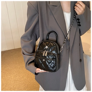 Détail d'un sac bandoulière matelassé noir avec chaîne porté sur une veste de blazer grise