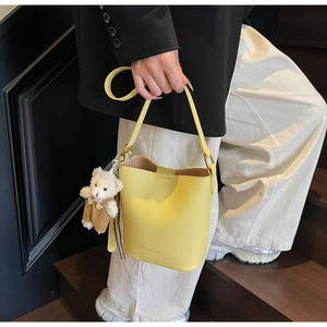 Detail of yellow lychee leather bucket bag with fashion debossing and teddy bear charm