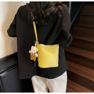 Bright yellow lychee grain bucket bag with teddy bear charm shown as crossbody on a model
