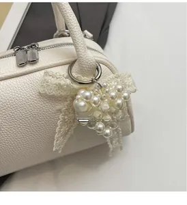 Dettaglio borsa a cilindro in pelle bianca con ciondolo a cuore di perle e fiocco