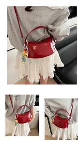 Detail view of red glossy saddle cloud bag with cute doll charm and pearl chain