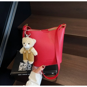 Detail view of red lychee textured bucket bag with a cute plush bear pendant accessory