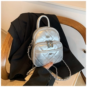 Détail d'un mini sac argenté matelassé avec chaîne posé sur une chaise en bois