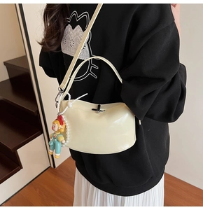 Detail view of cream white crescent hobo bag with a cute doll charm and pearl strap