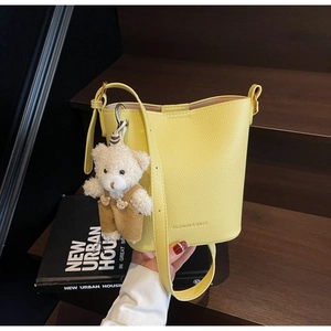 Close-up of a yellow bucket bag with litchi texture and a cute teddy bear charm
