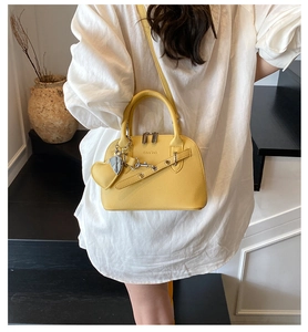 Chic yellow leather shell bag with heart charm shown in a lifestyle street fashion scene