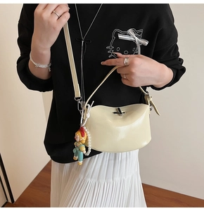 Detailed shot of cream patent leather handbag with silver clasp and cute doll pendant