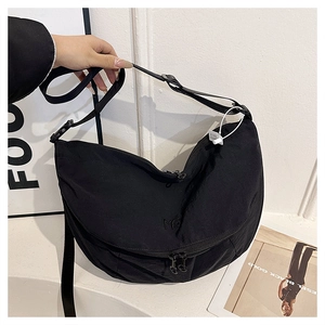 Detail of black nylon crescent crossbody bag featuring dual zippers and ME embroidery