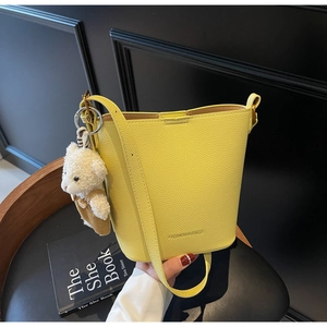 Detail view of yellow lychee grain bucket bag with cute bear charm on a dark chair