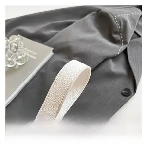 Close-up of a white pebble leather strap with precise stitching on a trendy crossbody bag