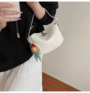 Detail of white glossy saddle bag featuring a silver twist lock and pearl doll charm
