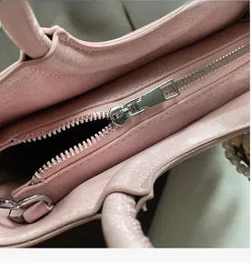 Close-up of pink lychee leather handbag featuring a smooth silver metal brand zipper