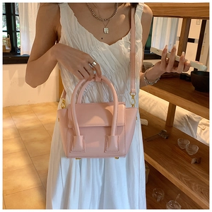 Sac seau en cuir rose pâle avec poignées et détails dorés présenté dans un cadre chic