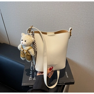 Detail of white litchi pattern bucket bag with a cute plush bear keychain on a sofa