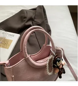 Pink bucket bag with pearl strap and cartoon charm displayed on a brown blazer with a book