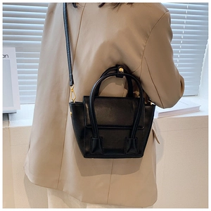 Détail d'un sac à main élégant en cuir noir avec ferrures dorées sur un blazer beige