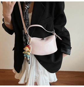 Detail of pink glossy crossbody bag with pearl chain and cartoon doll on a model