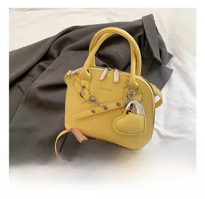 Macro detail of yellow leather shell bag featuring heart charm and chain decoration