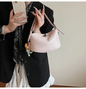 Detail of light pink crescent handbag with doll charm and pearl accessories