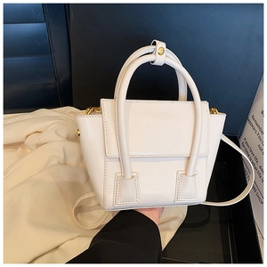 Détail d'un sac trapèze crème avec doubles poignées et des accessoires en métal doré