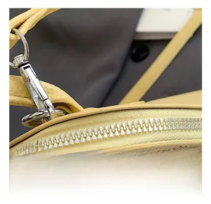 Close-up of silver metal lobster clasp and smooth zipper on light yellow leather bag