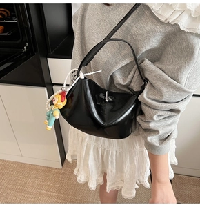 Detail of black glossy faux leather crescent bag with silver lock and pearl charm strap