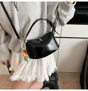 Detail of black glossy crescent crossbody bag with silver rotating lock and charm
