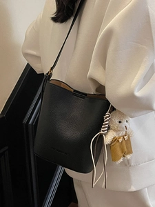 Chic black lychee grain leather bucket bag with a cute plush bear charm for daily wear