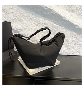 Detail of minimalist black crescent bag with ruffled shoulder strap on artistic books