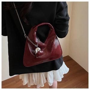 Detail of burgundy patent leather bag with silver chain and heart-shaped metal pendant