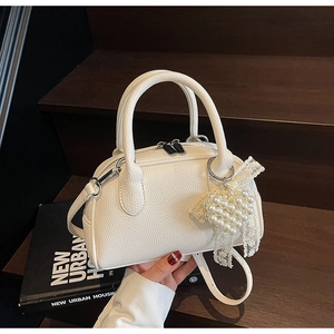 Dettaglio borsa boston in pelle bianca con ciondolo a cuore di perle e finiture in argento
