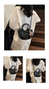 Detail of black PU leather crescent bucket bag with round handle and cartoon doll charm