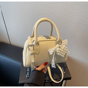 Dettaglio borsa bowling beige in pelle martellata con ciondolo a cuore di perle e fiocco