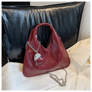 Detailed view of dark red glossy wrinkled leather handbag with silver chain and heart charm