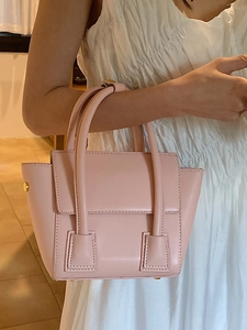 Sac seau élégant en cuir rose avec boucles dorées tenu par un mannequin en robe blanche