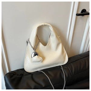 Macro detail of creamy white triangle bag featuring crinkled texture and silver heart charm