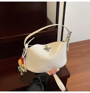 Detail view of cream half-moon handbag with silver metallic twist lock and pearl charm
