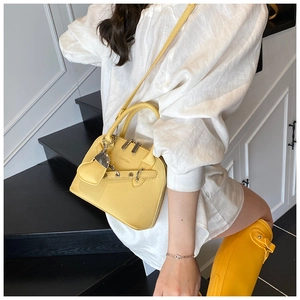Detail of yellow shell bag featuring litchi texture leather and brand logo engraving