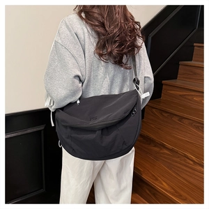Minimalist black crescent crossbody bag with ME embroidery detail on light nylon fabric