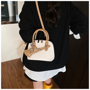 Detail of cream shell handbag with brown handles, pebble leather texture and heart charm