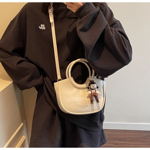 Chic cream-colored bucket bag with adjustable strap and cute plush charm detail