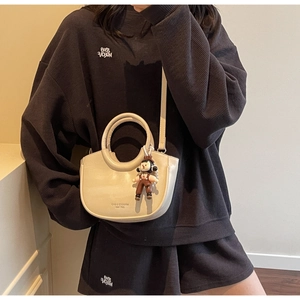Detail shot of a minimalist cream crescent bucket bag with cute brown doll pendant