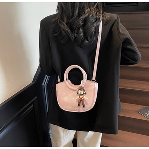 Detail view of pink bucket bag with pearl chain and cute cartoon doll charm accessory