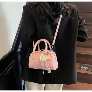 Dettaglio della borsa rosa in pelle litchi con fiocco di pizzo e perle indossata dal modello