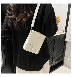 Detail of unique white blazer shaped box bag with decorative tie and wide shoulder strap