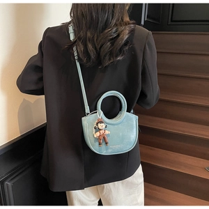 Detail of light blue crescent bucket bag with cute girl charm on a textured leather strap